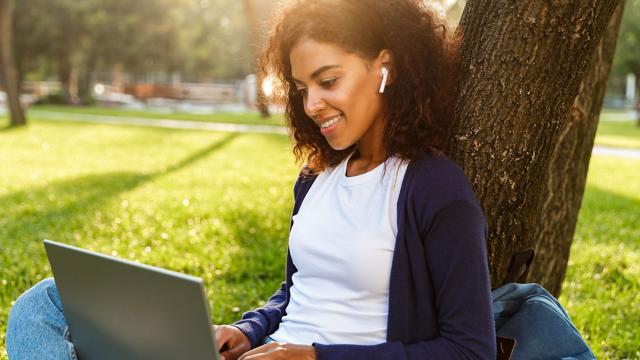 Young woman sitting outside listening to music while working on her laptop.