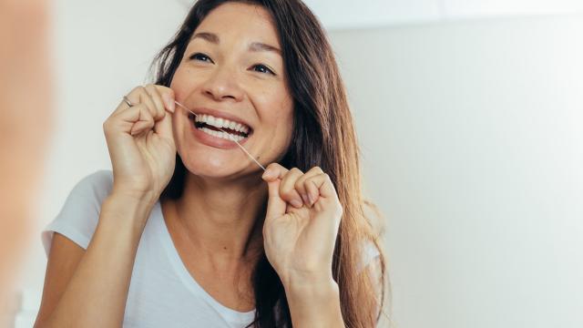 Woman flossing her teeth while looking in the mirror.