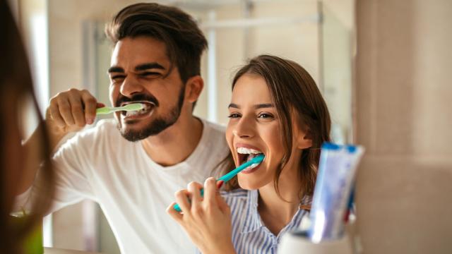 Young couple looking in the mirror while brushing their teeth together.