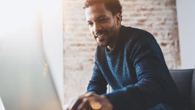 A man sits on a sofa and uses a laptop. 