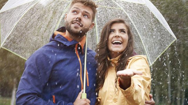 A couple stands under an umbrella in the rain. 