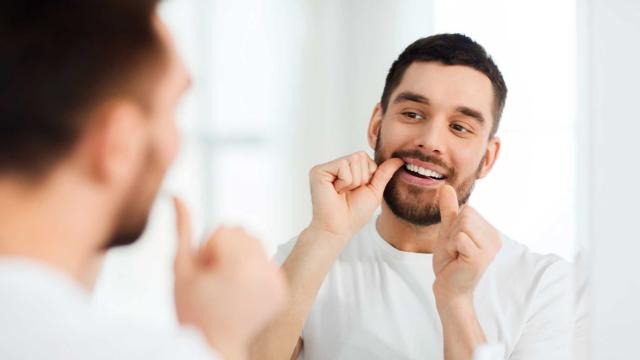 A man looks in a mirror while flossing his teeth. 