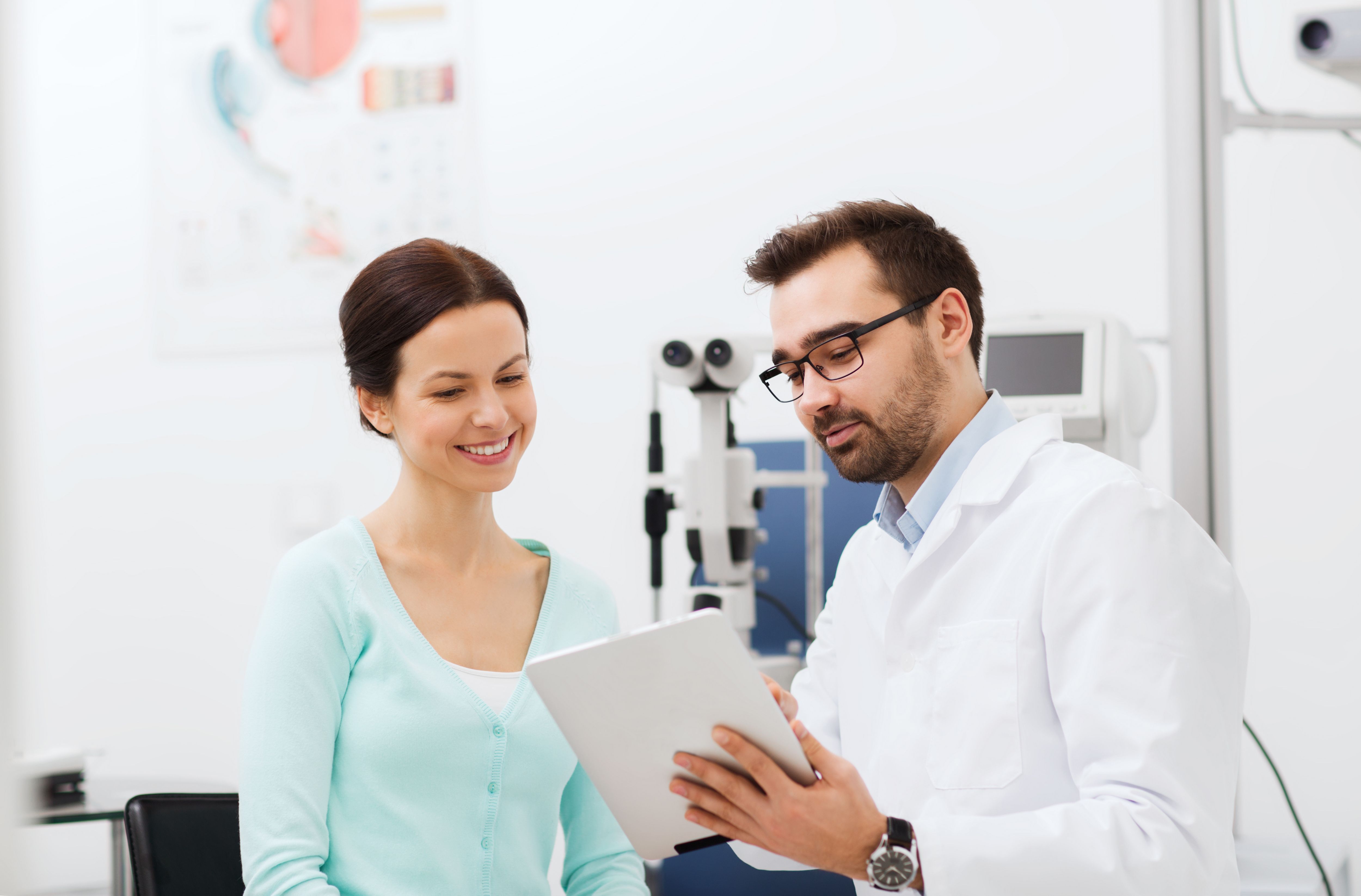 health care, medicine, people, eyesight and technology concept - optician in glasses with tablet pc computer and patient at eye clinic or optics store