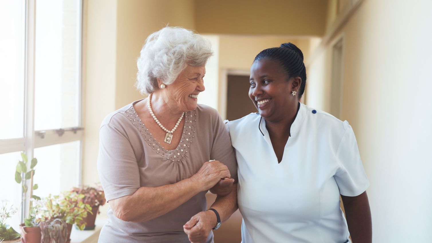 Medical provider and patient share a smile as they walk arm-in-arm down the hall.