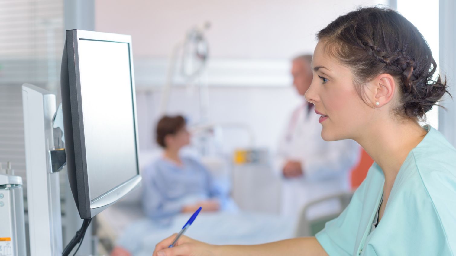 A medical assistant sits at a computer while filling out a form