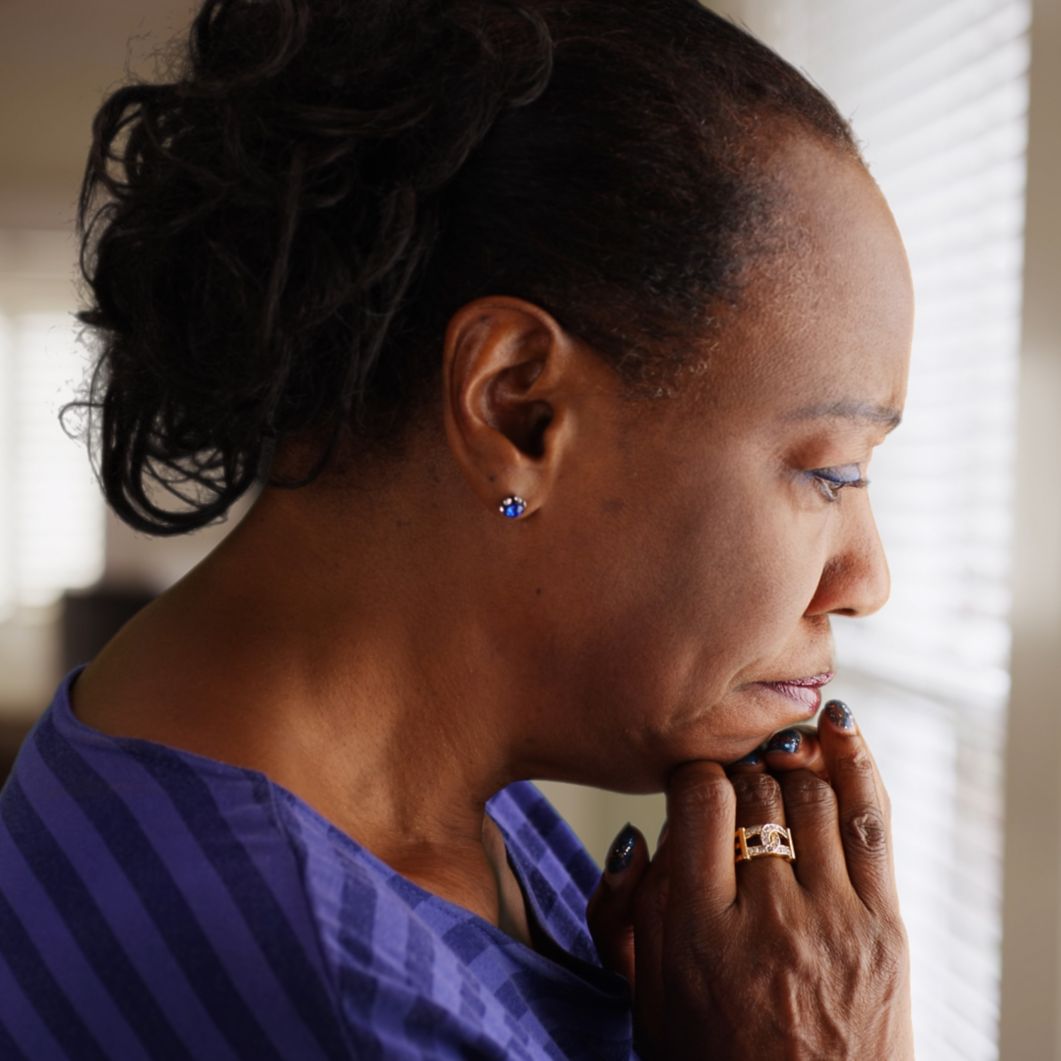 An older black woman mournfully looks out her window