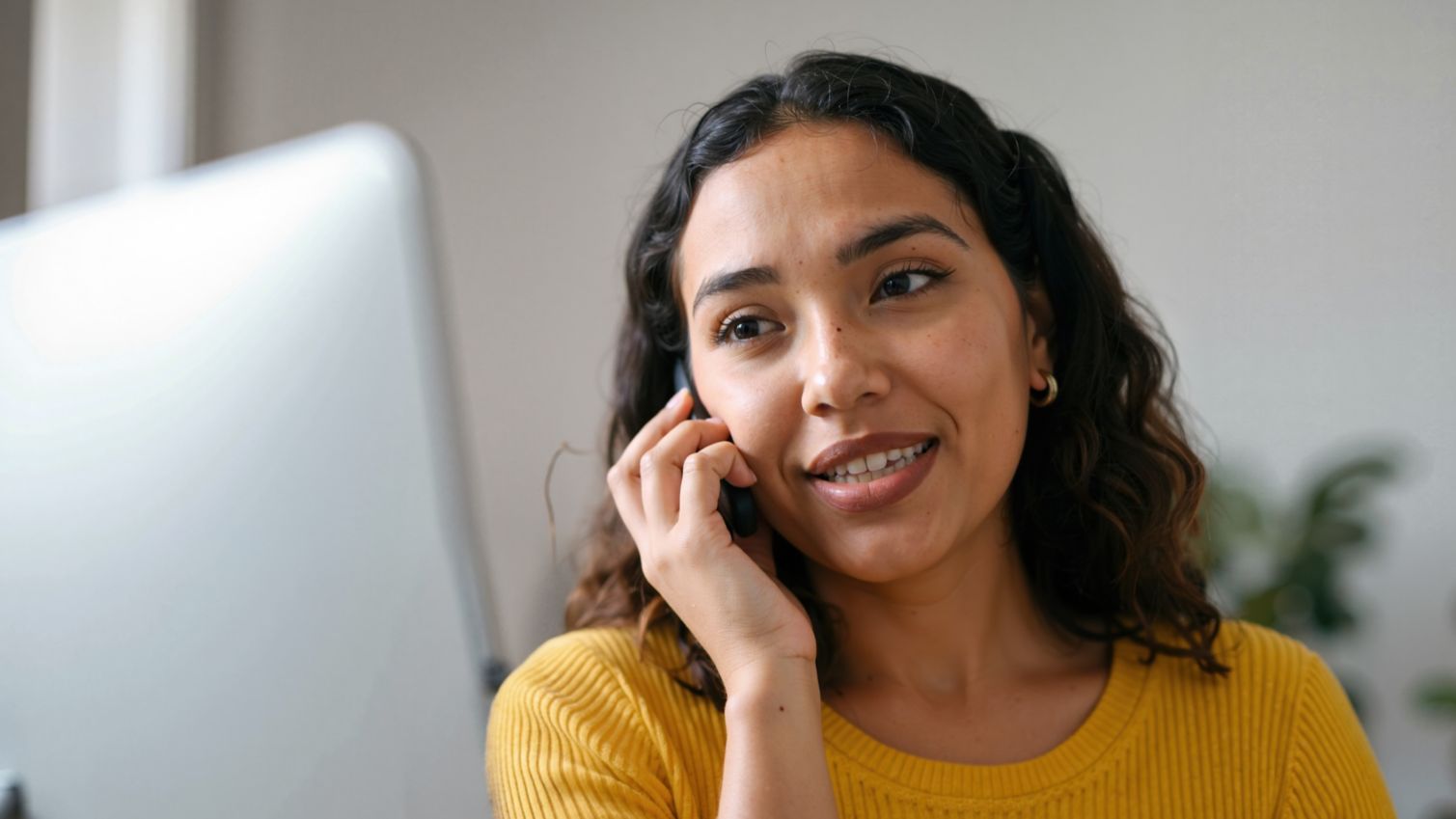 A woman talking on smartphone and working on computer at home