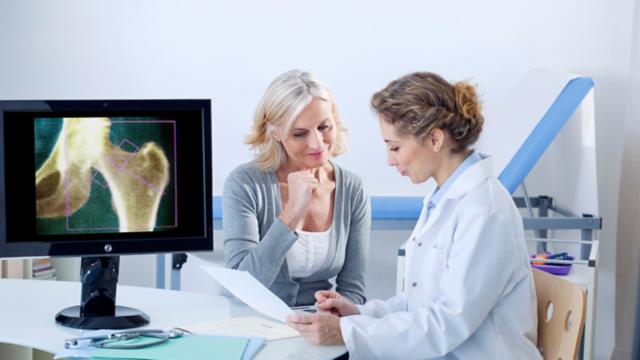 A woman talks to her doctor near an X-ray image of a hip joint.