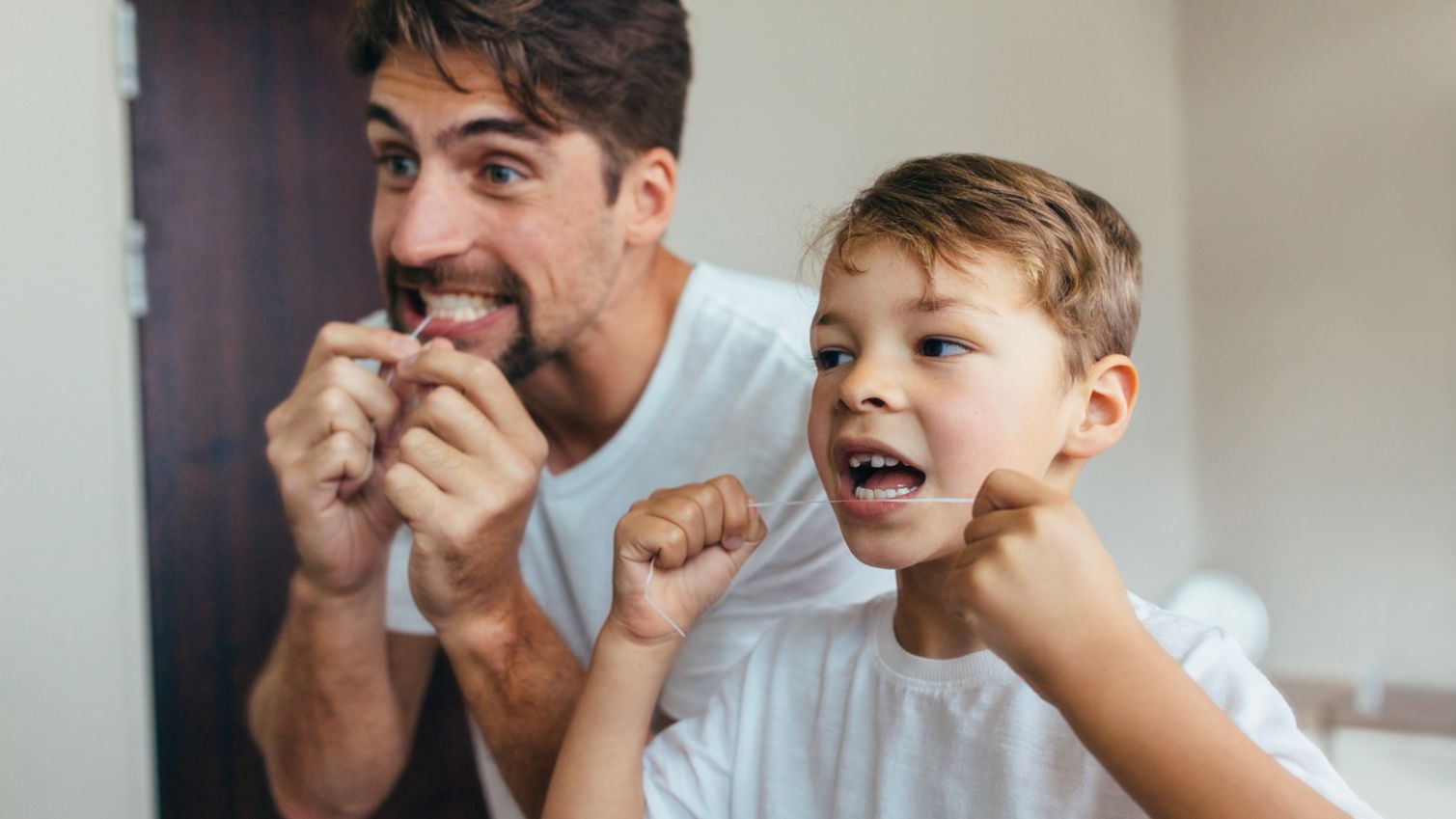 Father and son flossing their teeth together.