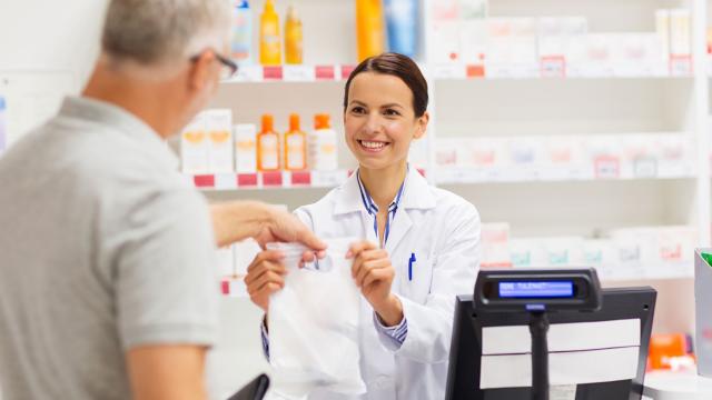A pharmacist hands a prescription to a customer. 