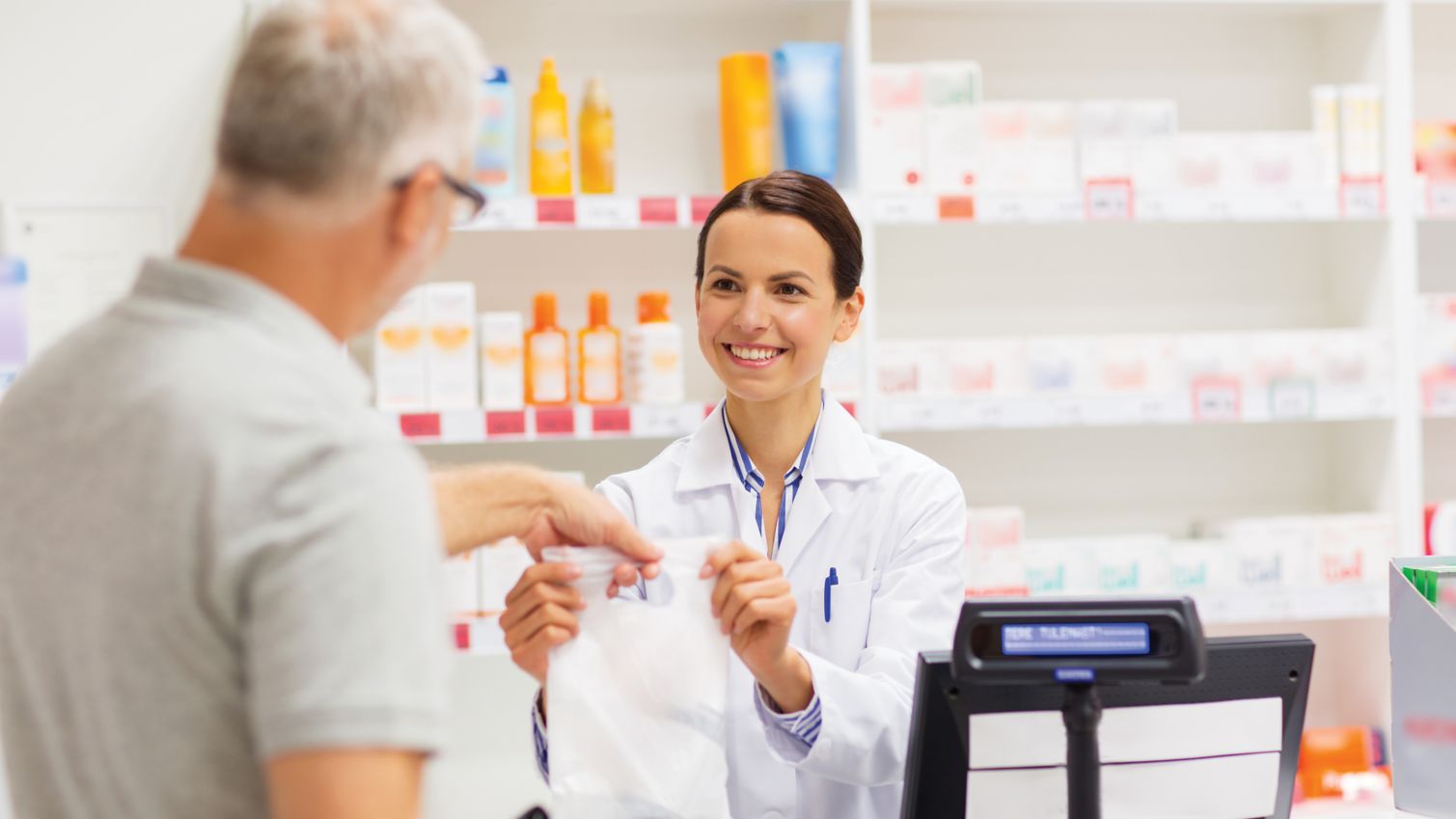 medicine, pharmaceutics, health care and people concept - female apothecary giving senior male customer his purchase in bag at drugstore