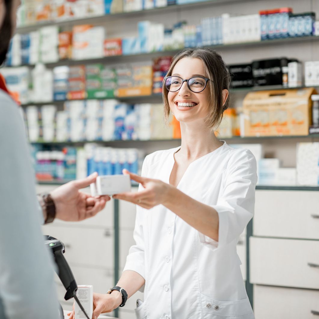 A pharmacist smiles as she hands a package to a customer. 