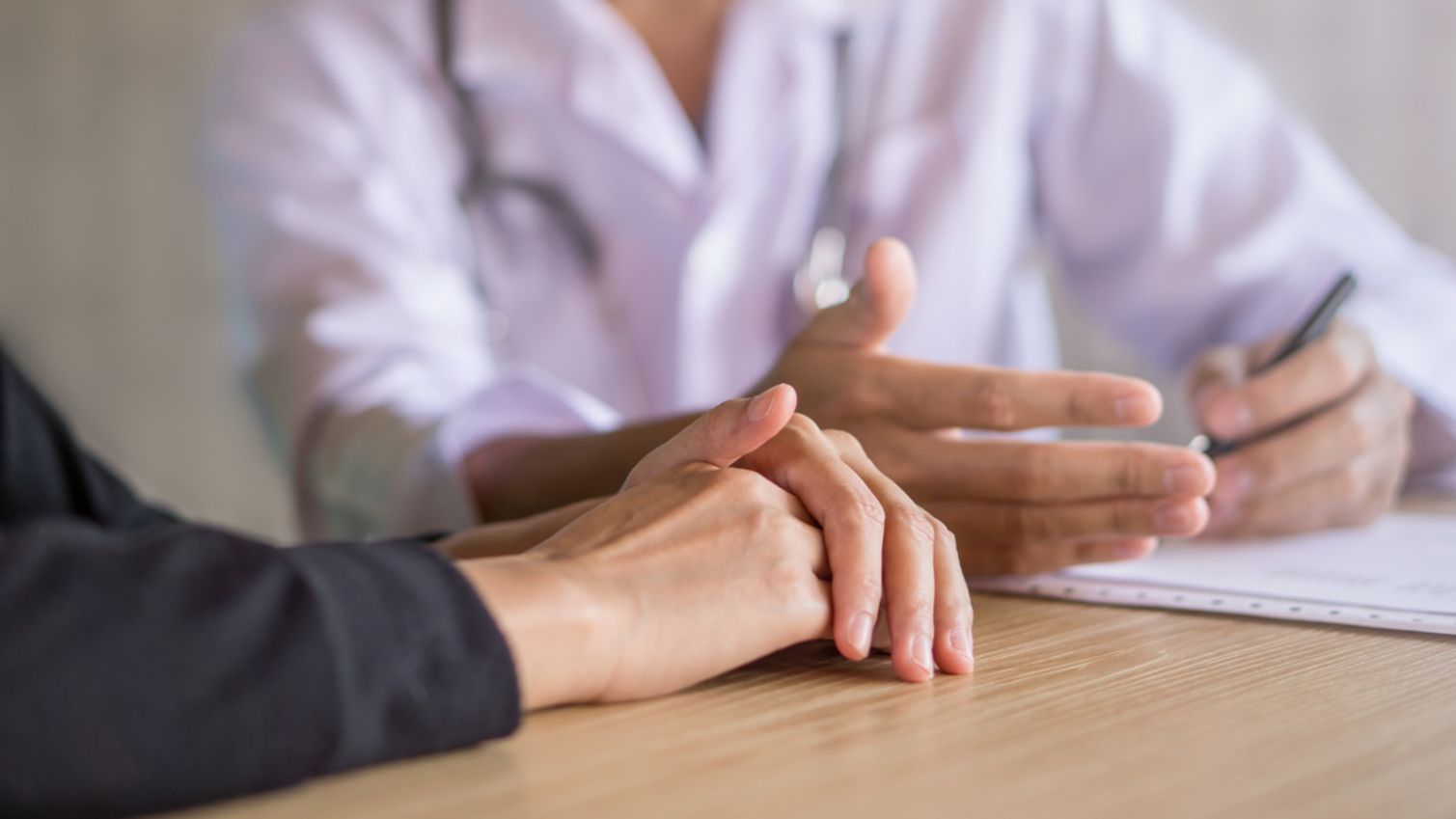 A doctor takes notes on a pad while talking to a patient.