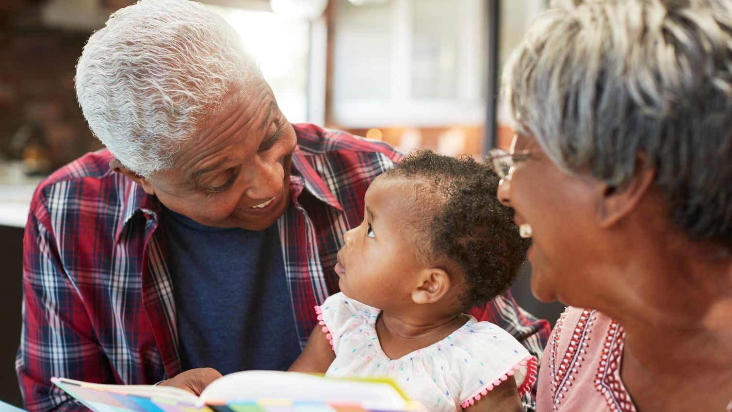 Grandparents read a book to their baby granddaughter at home.