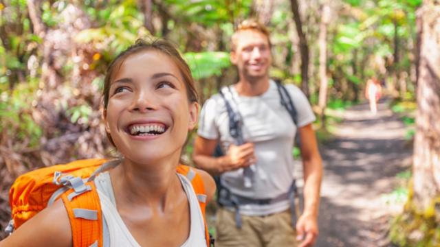 A man and woman backpack through a forest.