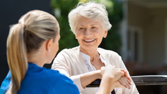 Smiling senior patient sitting on wheelchair with nurse supporting her.