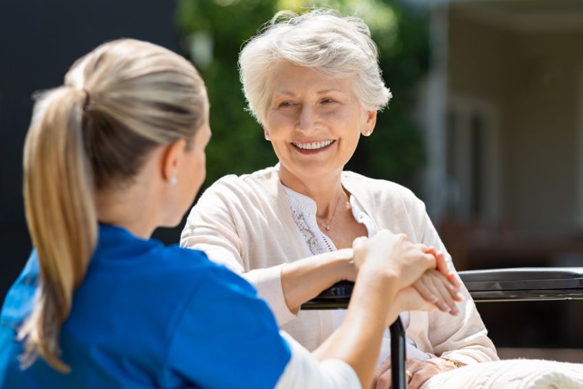 Smiling senior patient sitting on wheelchair with nurse supporting her.