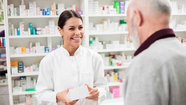 A pharmacist smiles as she gives a customer his prescription. 