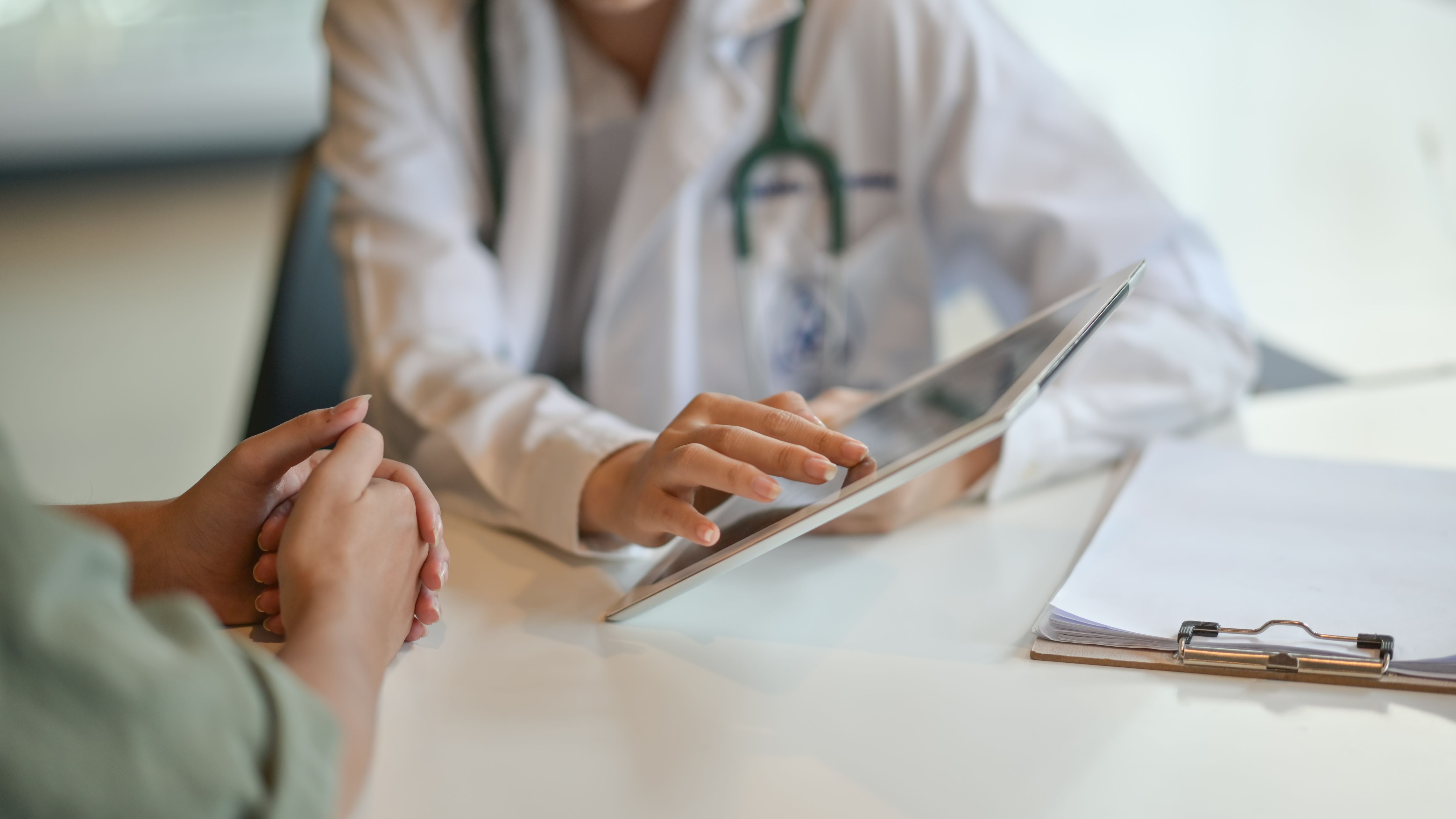 Doctor uses a tablet while speaking to a patient.