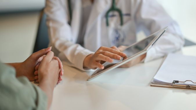 Doctor uses a tablet while speaking to a patient.