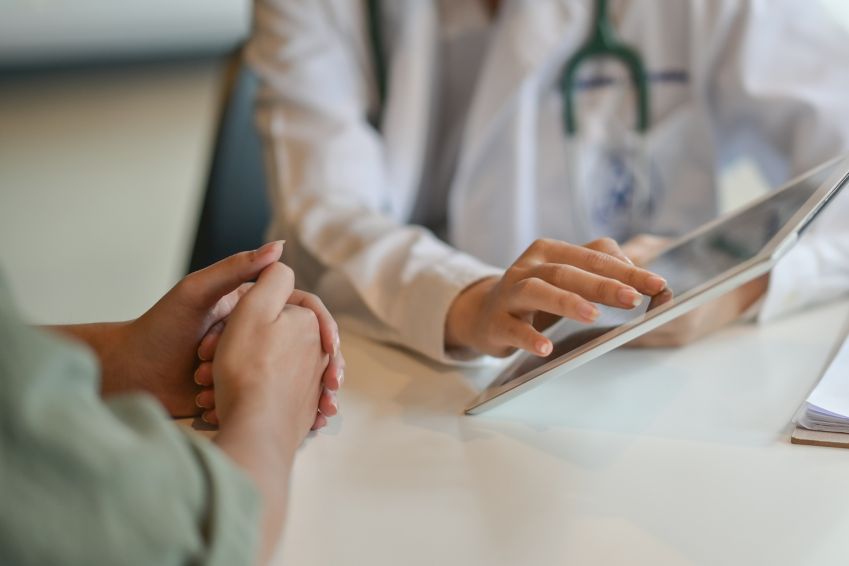 Doctor uses a tablet while speaking to a patient.