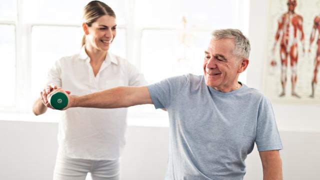 A physical therapist helps a man work out at a rehab center.