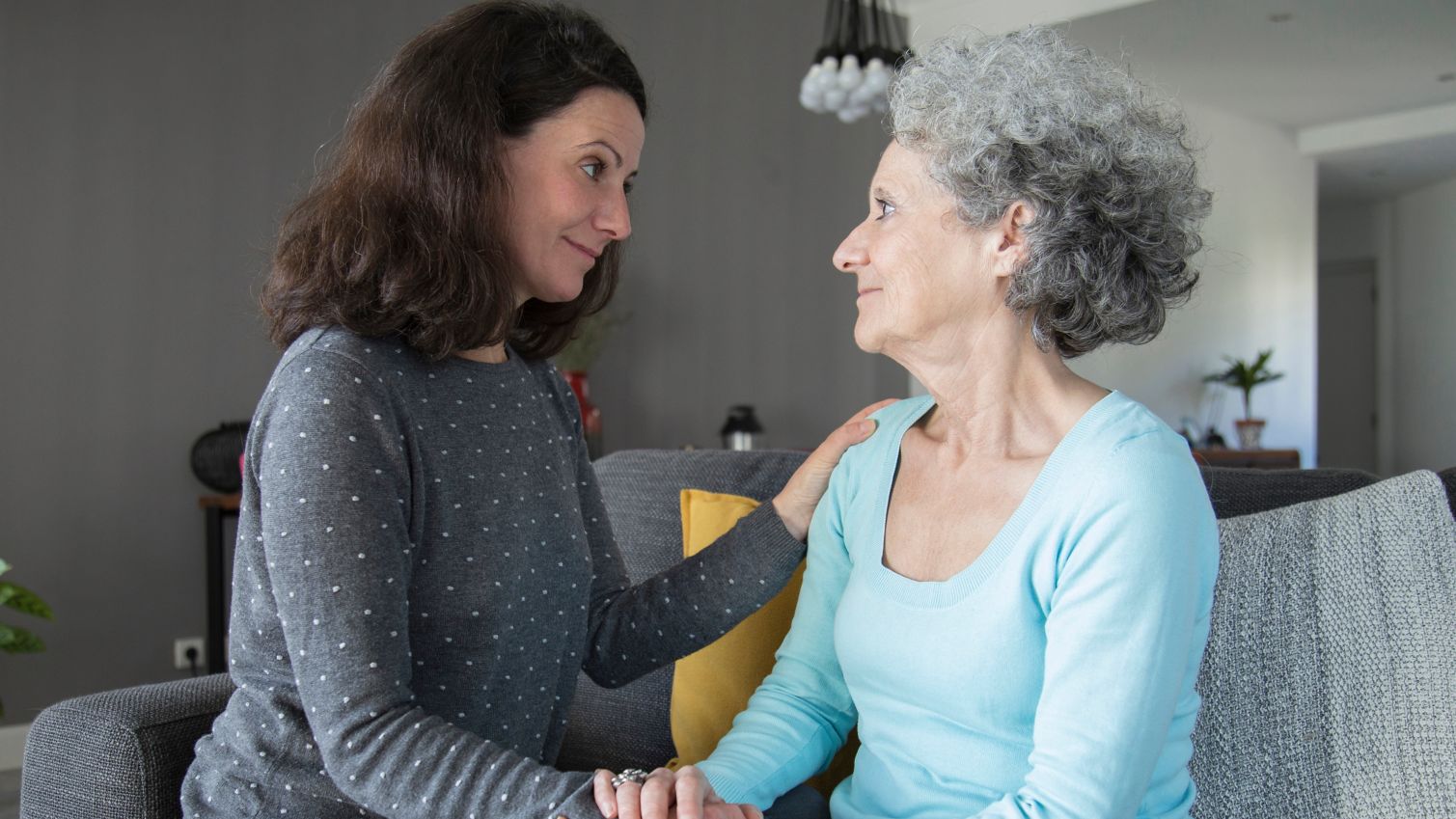 Mother and daughter sitting on couch holding hands and looking at each other.