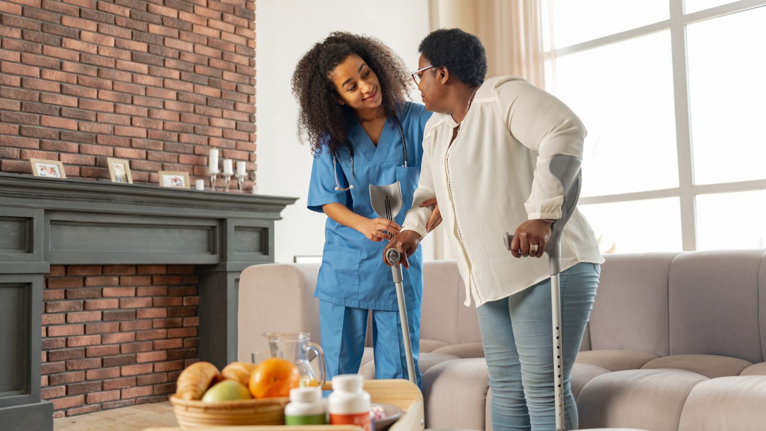 Young female nurse helps older woman patient use forearm walkers.