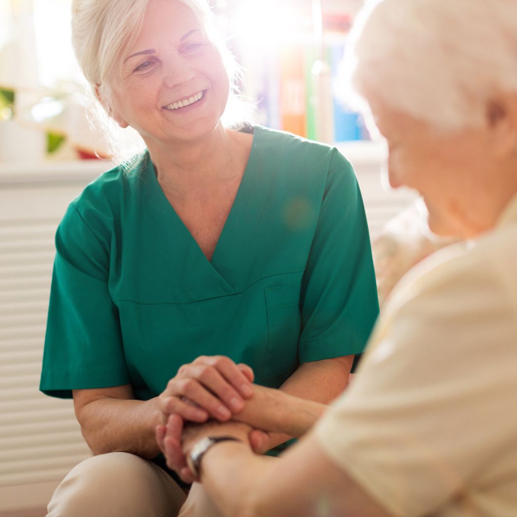 Nurse smiling and holding hands with her patient.