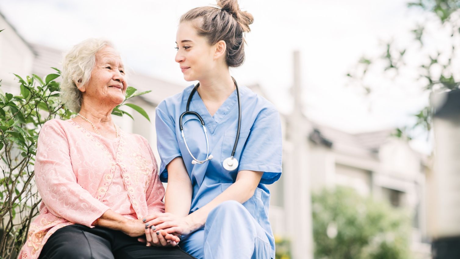 A woman smiles as her caregiver sits with her outside. 