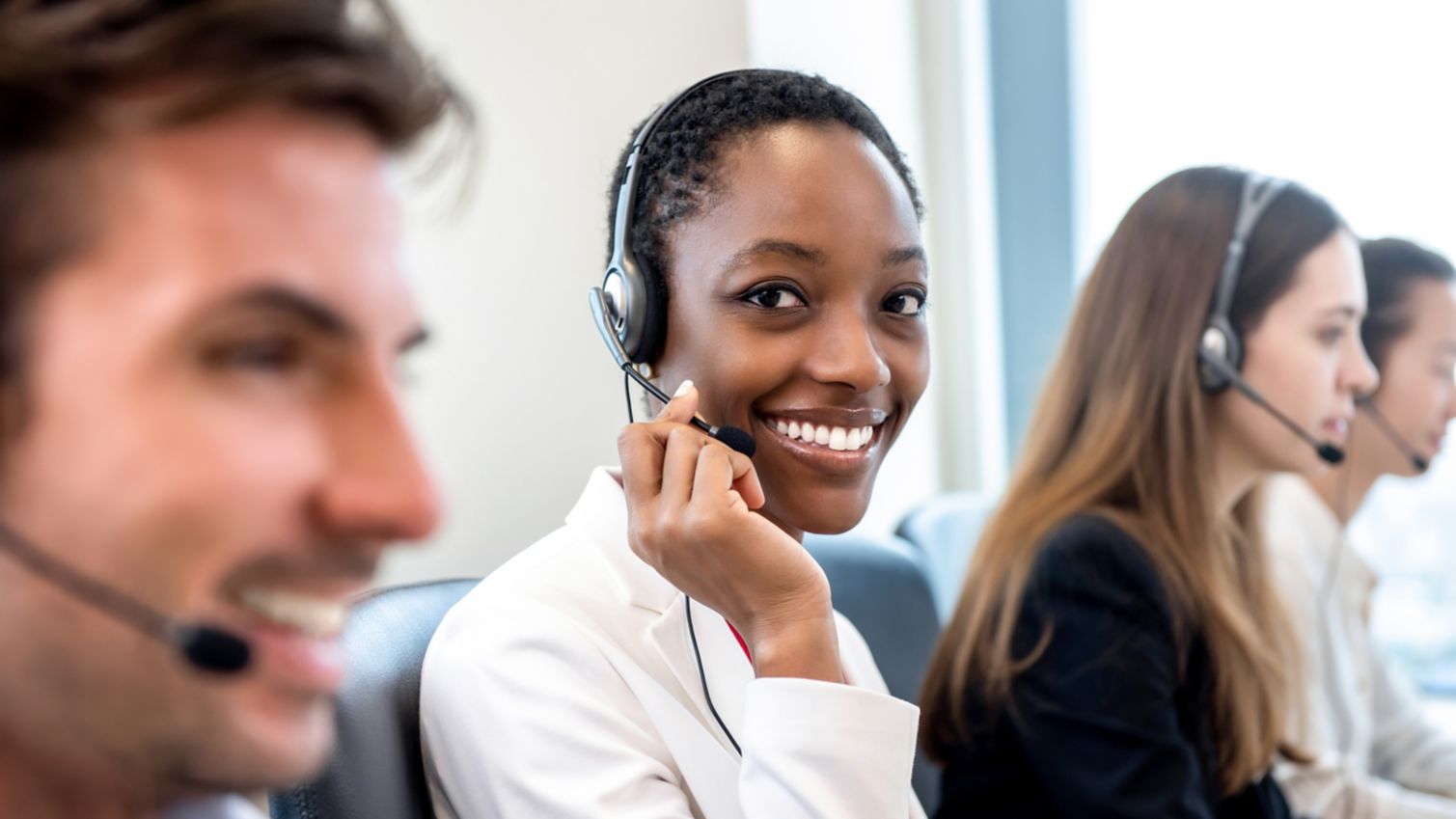 Smiling beautiful African American woman working in call center office with diverse team as the customer care operators