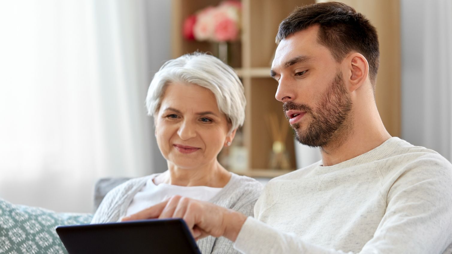 Young man uses tablet with older woman.