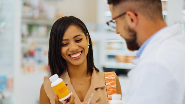 Smiling woman holds a pill bottle and talks to a pharmacist.