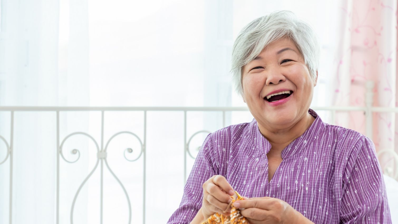 A woman laughs while knitting. 