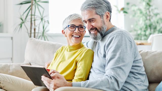 A woman smiles up at her husband who is looking at a tablet. 