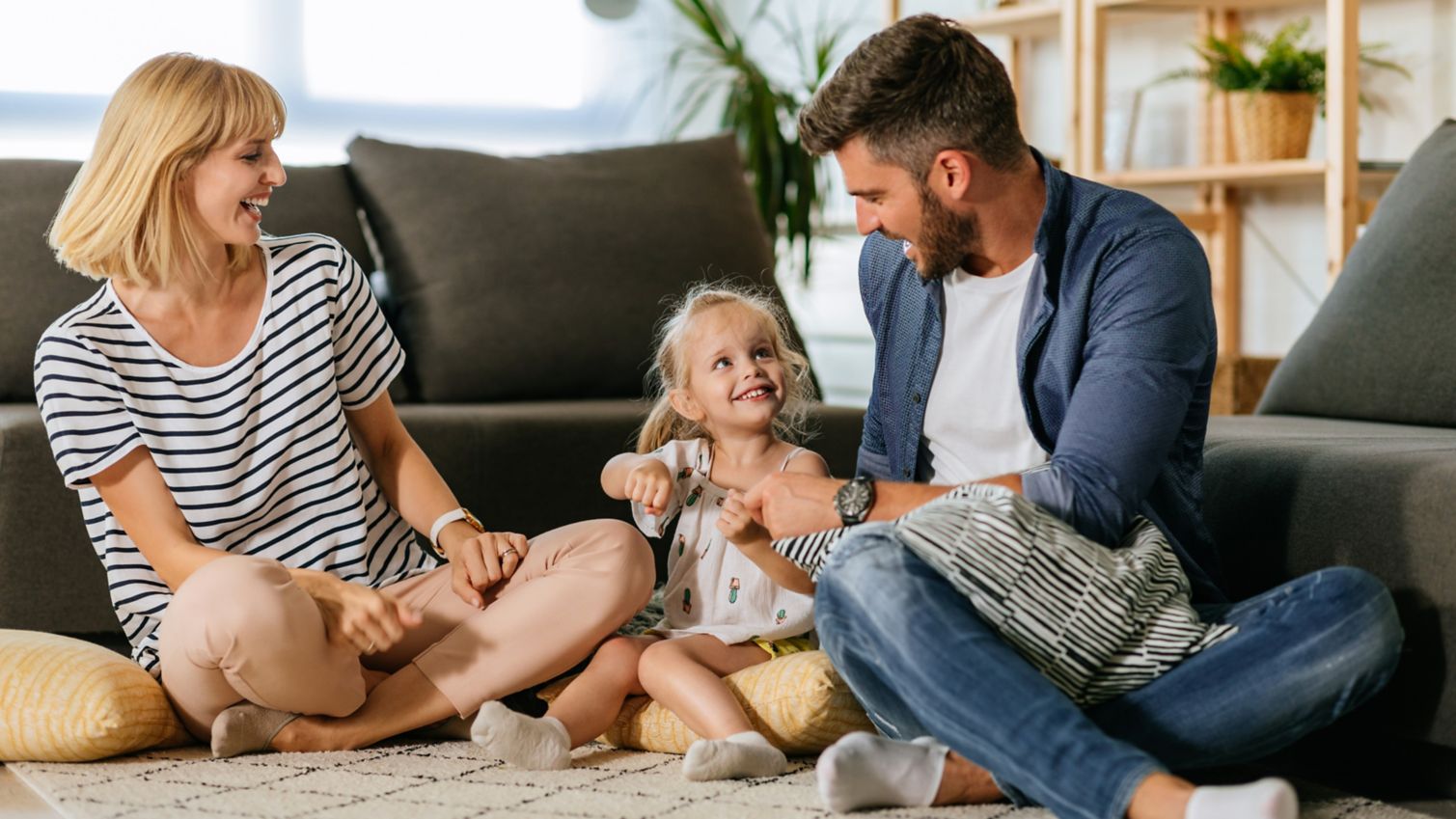 Husband and wife playing with young daughter on floor.