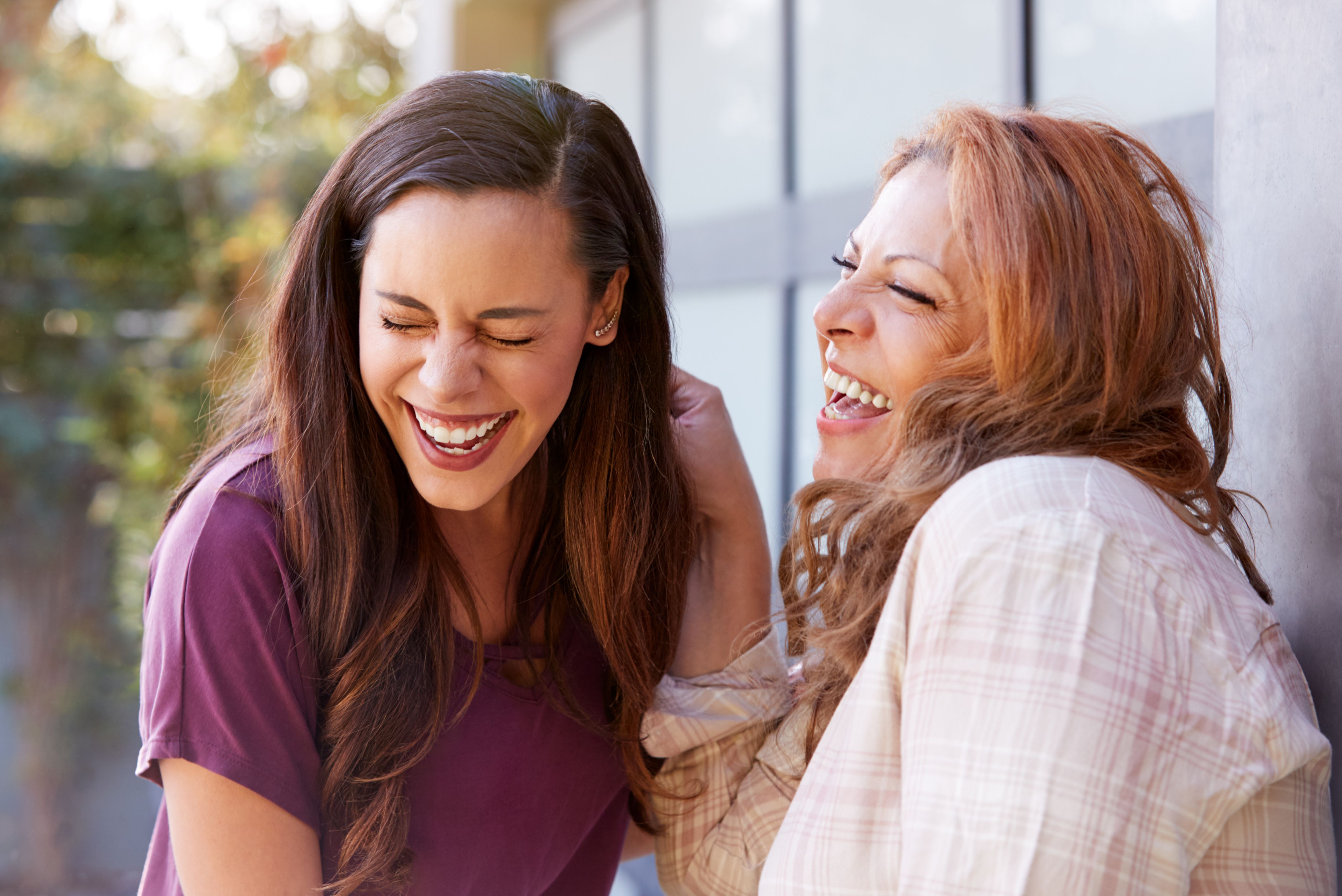 Senior Hispanic Mother Talking And Laughing With Adult Daughter In Garden At Home