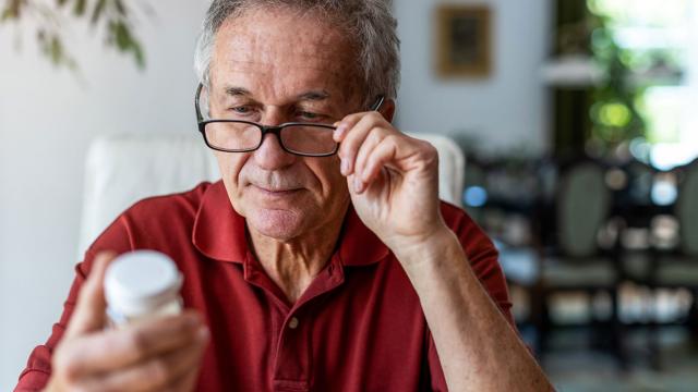 A man adjusts his glasses as he reads a prescription bottle. 