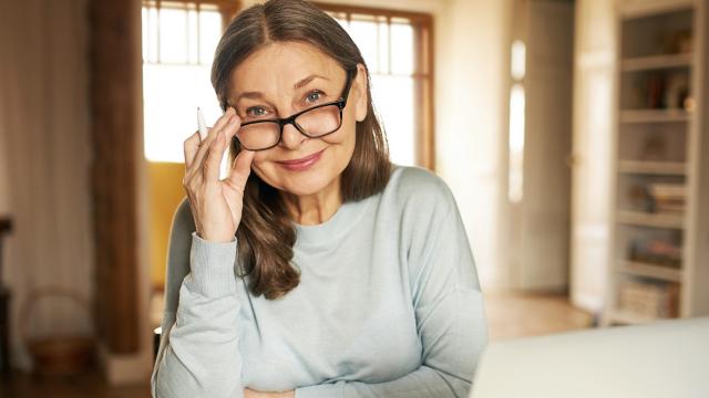 A woman smiles at the camera while adjusting her glasses. 