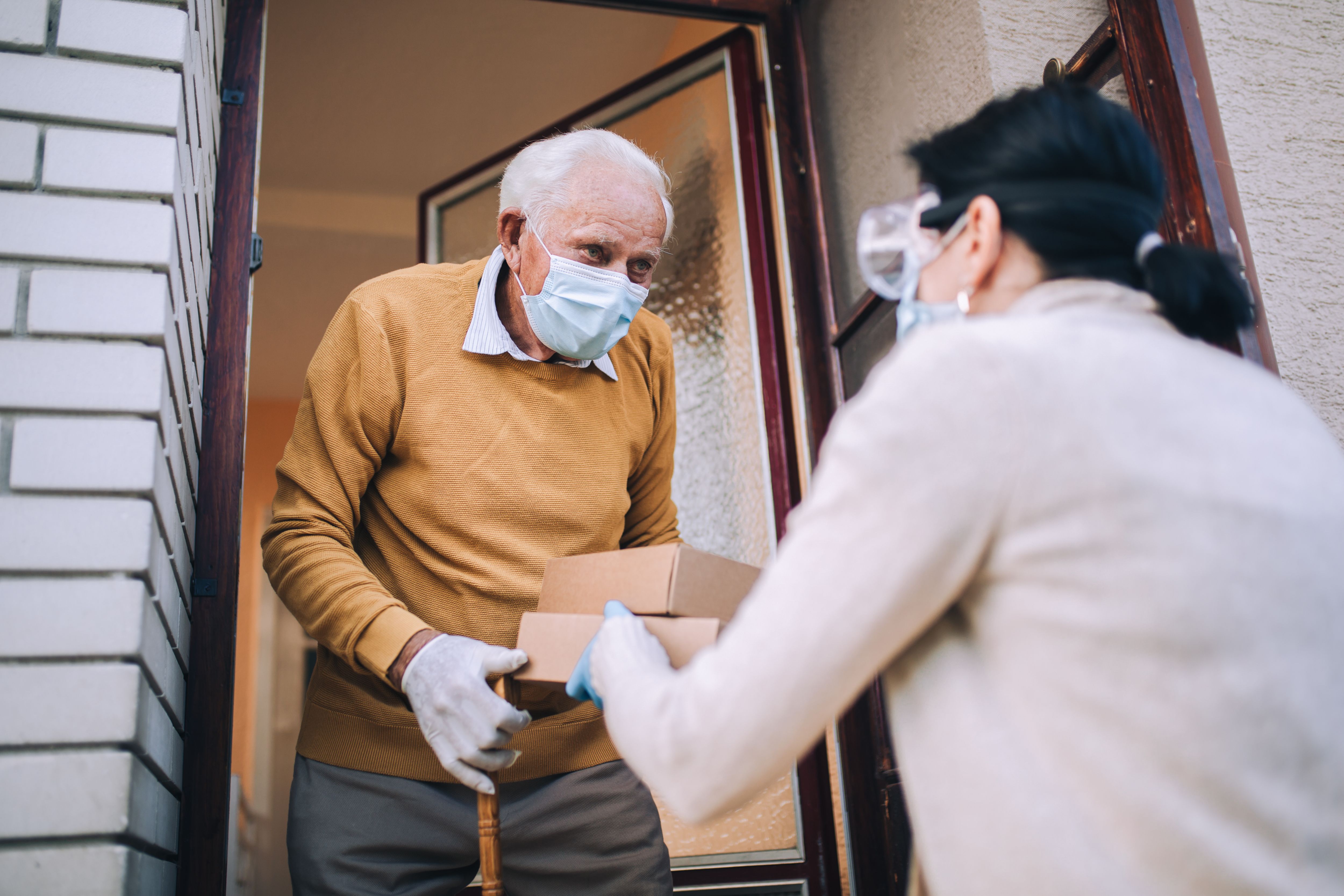 Young female volunteer in mask gives an elderly man boxes of food