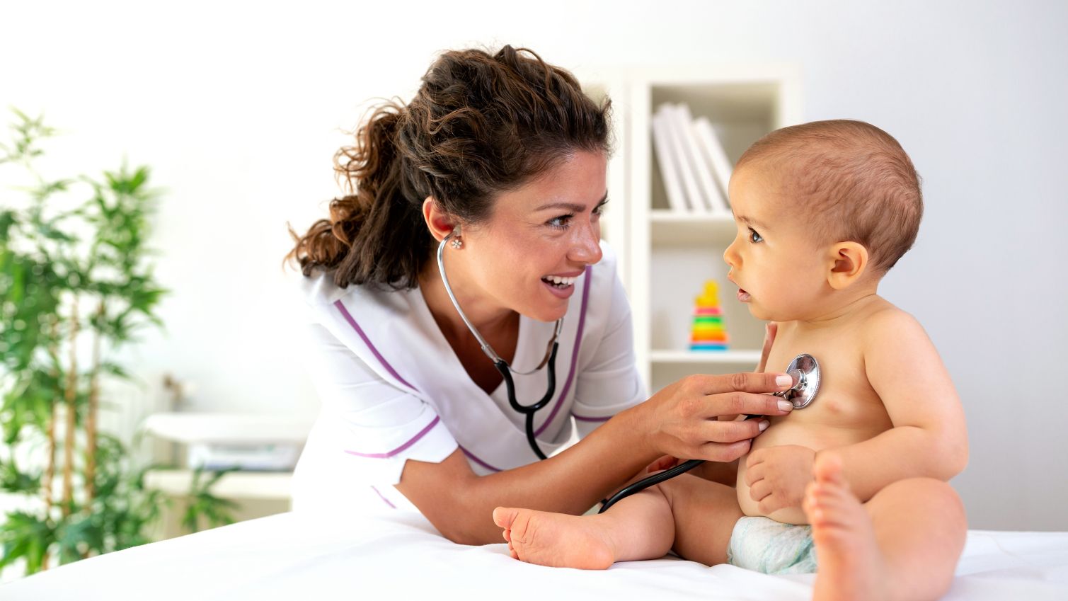 Female health care provider holds smiling baby during a well-child exam