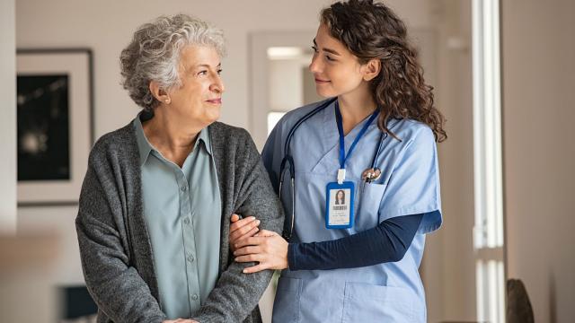 Female nurse assisting older female to walk.