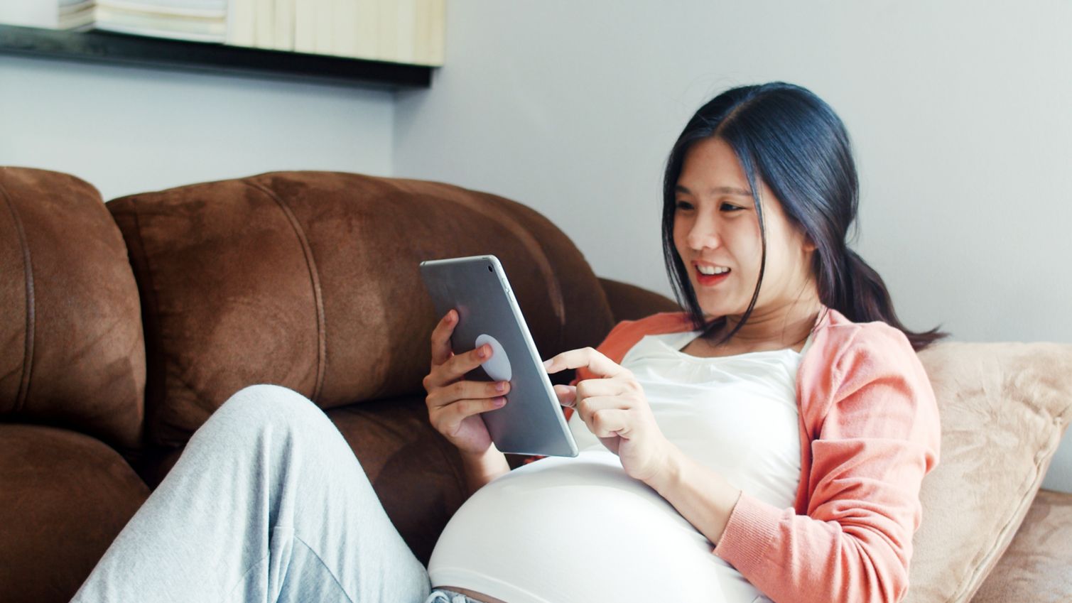 Adult laying on a couch and reading a tablet.