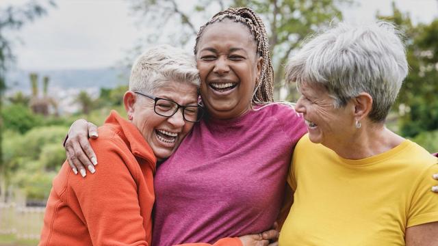 Three women laugh and hug at a park. 