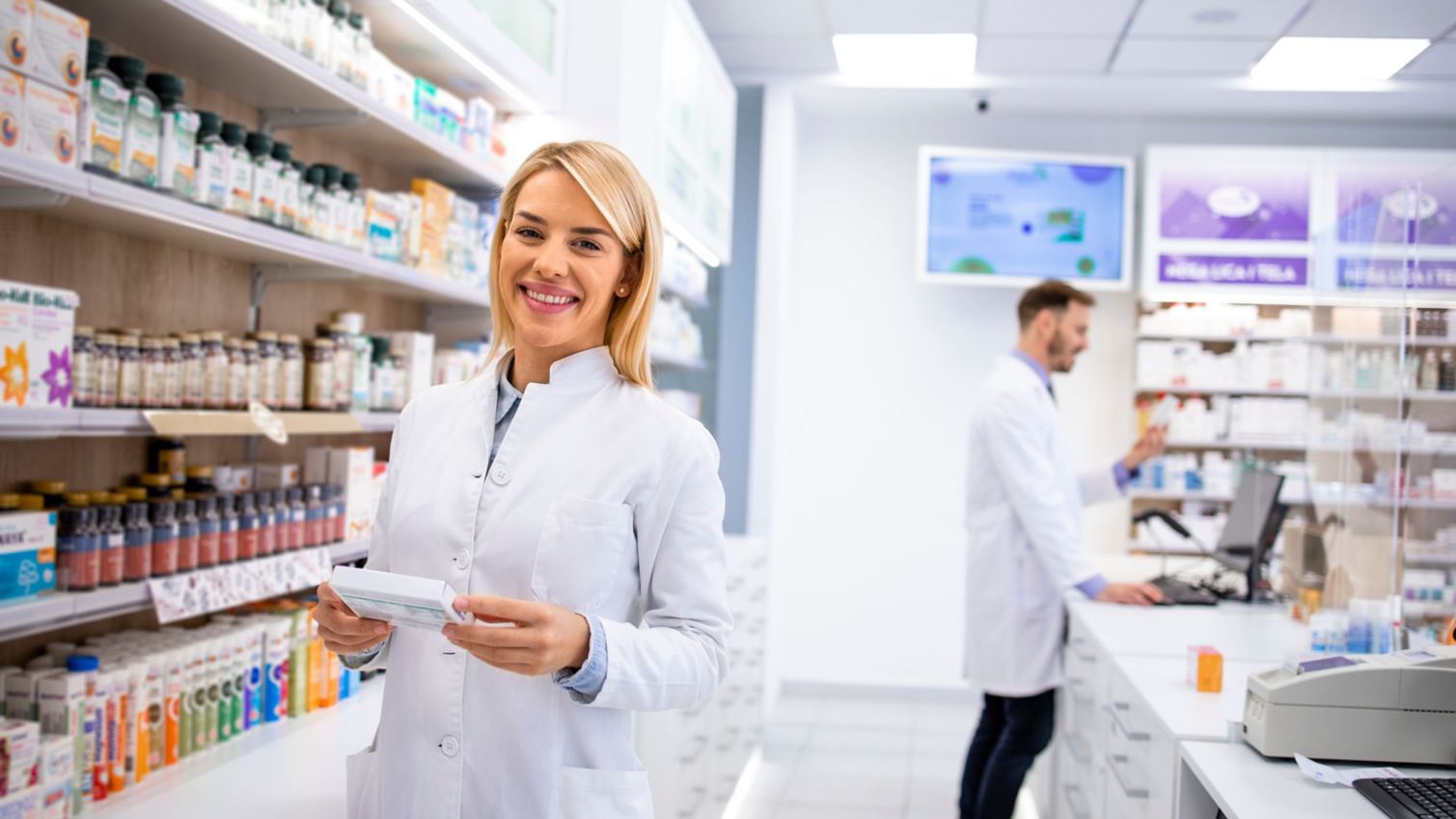 Smiling female pharmacist holding a box of medication.