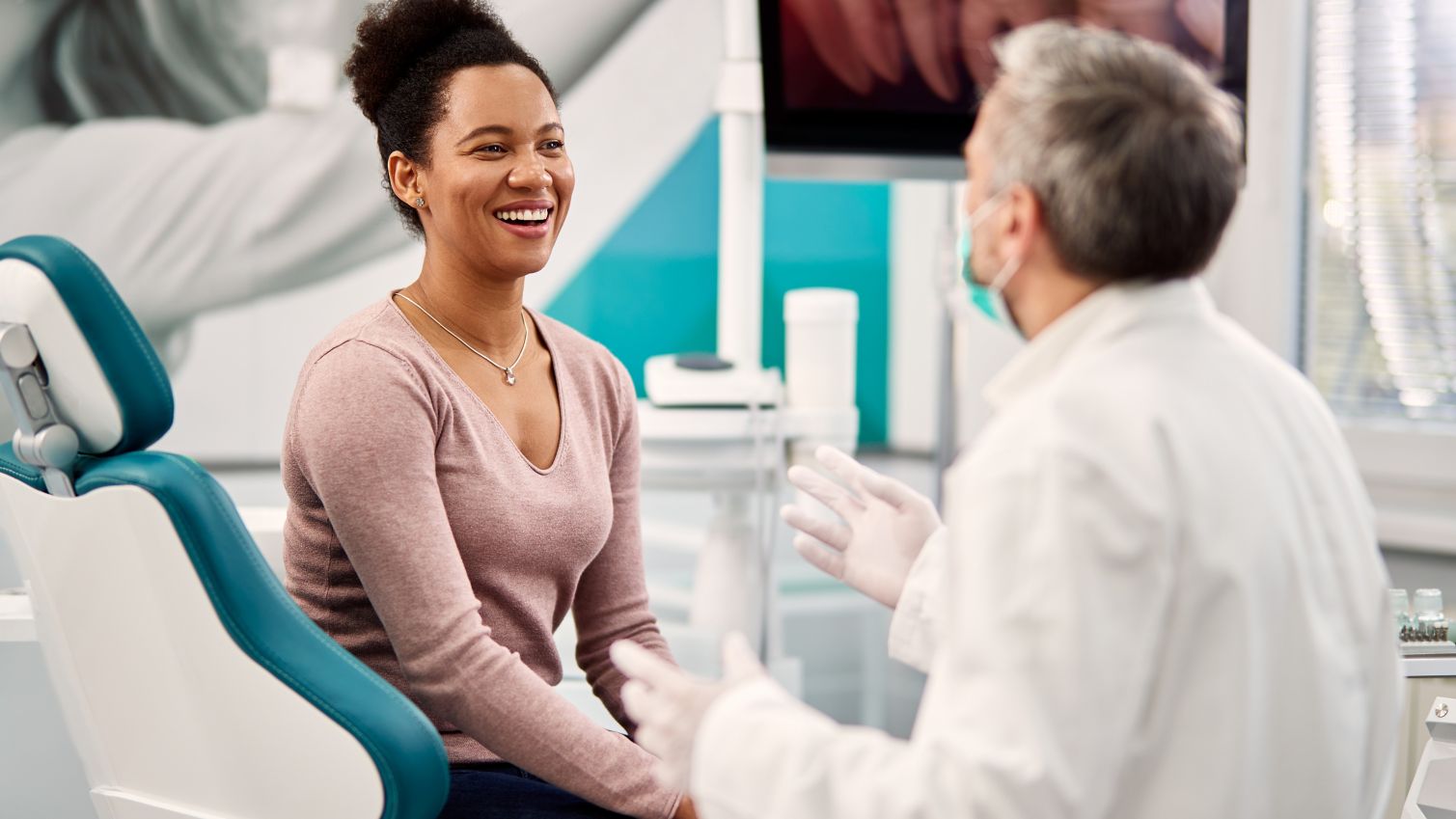 A woman in a dentist's office smiles while talking to her provider. 