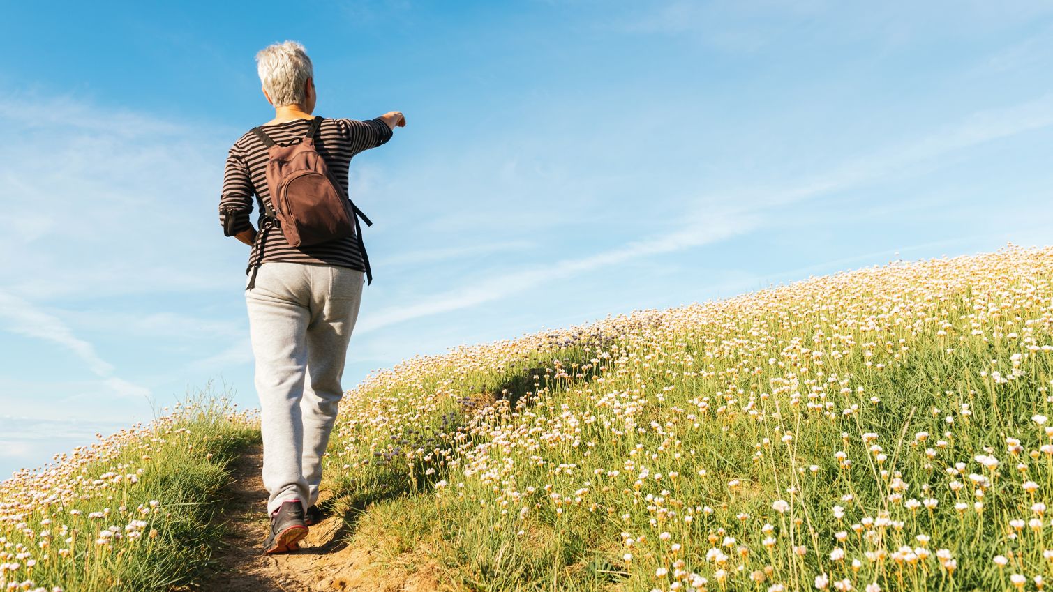 A hiker is seen from behind as she walks up a trail hill. 