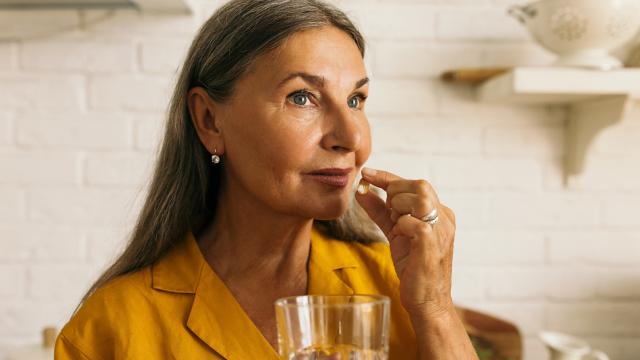 A woman takes a pill with a glass of water. 