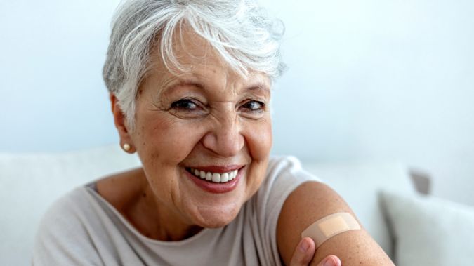 Proud senior woman smile after vaccination with bandage on arm.