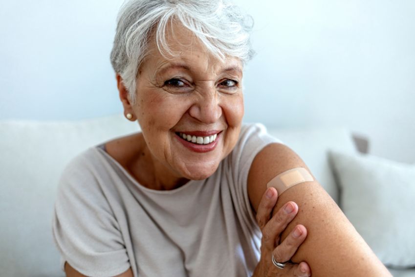 Proud senior woman smile after vaccination with bandage on arm.